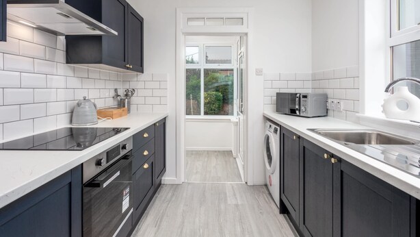 A compact kitchen with dark cabinets, white countertops, a built-in microwave, and a window providing natural light.