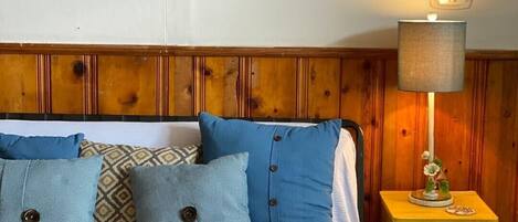 A bedroom with a wooden headboard, a bed with blue bedding, and a nightstand with a lamp.