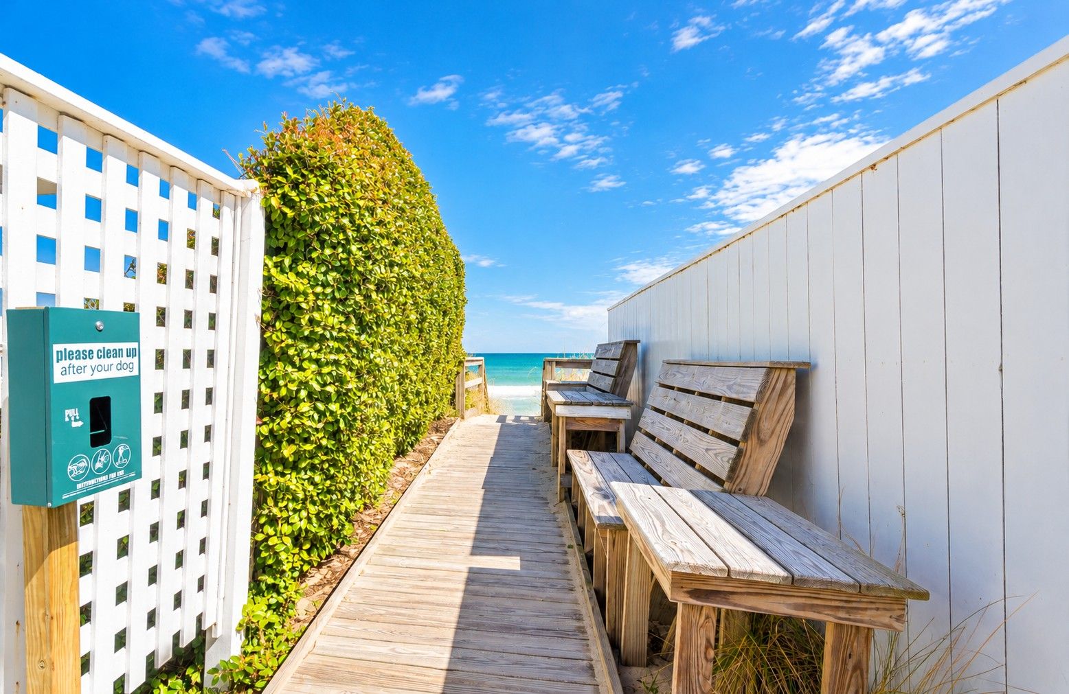 A wooden pathway leading to beachside seating with a 'please clean up after your dog' sign.