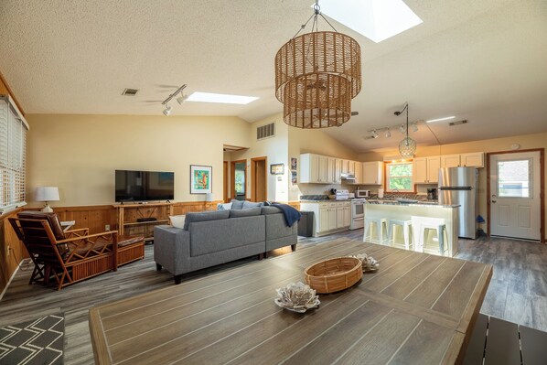 A spacious living area with a sofa, a television, and a dining table. - Coker Cabana - Duck, Carolina Dunes, Oceanside, 400 Yds to Beach, Sound Access, Flex Stays (Duck)