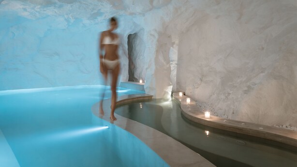 Un área de spa con piscina azul, paredes de piedra y velas.