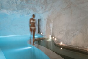 A spa area with a blue pool, stone walls, and candles. - Lovia Mykonos (Mykonos)