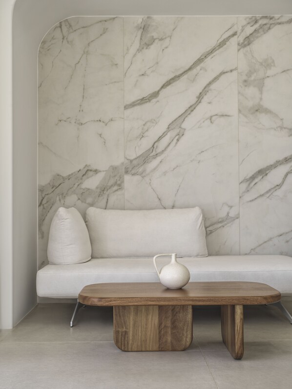 A modern interior with a marble-patterned wall, a white sofa, and a wooden coffee table with a white vase. - Lovia Mykonos (Mykonos)
