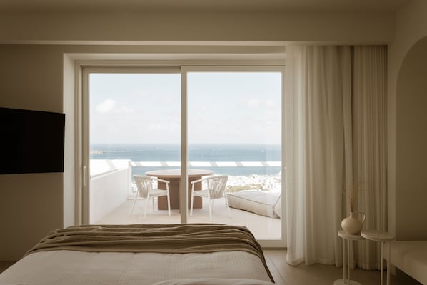 A hotel room with a bed, a balcony with a table and chairs, and a view of the sea. - Lovia Mykonos (Mykonos)