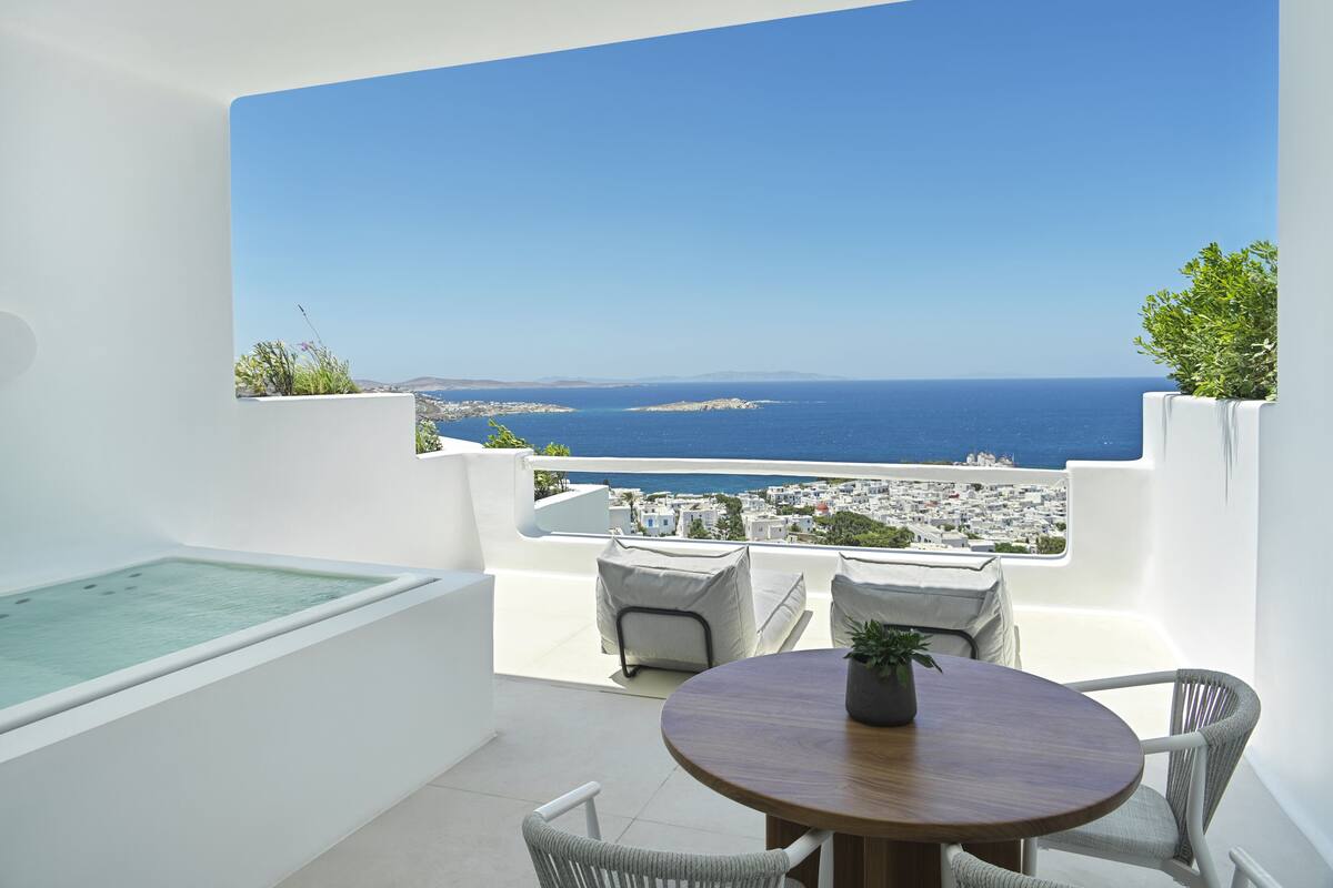 A balcony with a view of the sea, a pool, and outdoor seating.