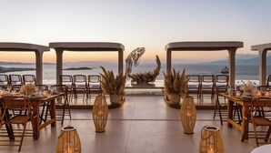 Un área de comedor al aire libre con mesas y sillas, un centro de mesa decorativo y vistas al océano.