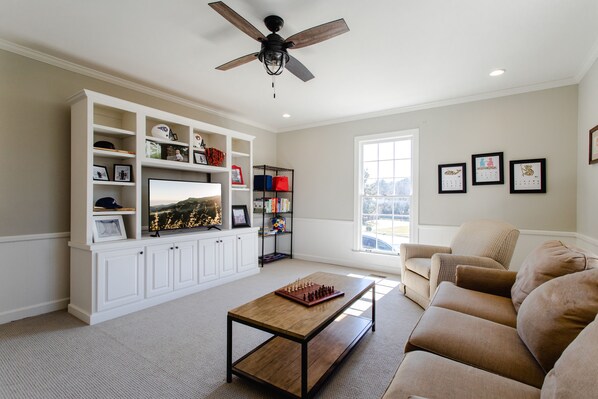 A living room with a wooden coffee table, white built-in shelving, a beige sofa, and a ceiling fan. - Above Nashville Harpeth Hills I Game Rm | Large Yard I Groups I Luxe Services (Nashville)