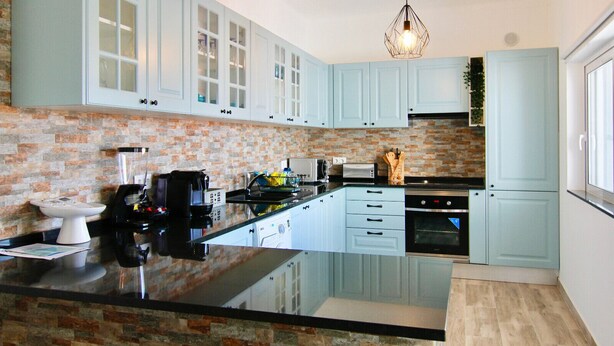 A modern kitchen with light blue cabinets, a brick backsplash, and a central island.