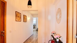 A hallway with wooden flooring, a black table with pink flowers, and a wall clock.