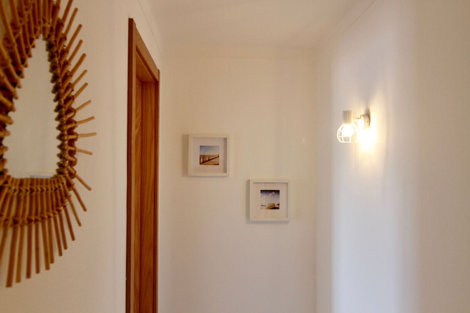 Un couloir avec une porte en bois, deux tableaux encadrés accrochés au mur et un luminaire fixé au mur.