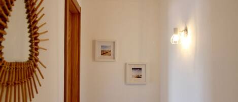 Un couloir avec une porte en bois, deux tableaux encadrés accrochés au mur et un luminaire fixé au mur.