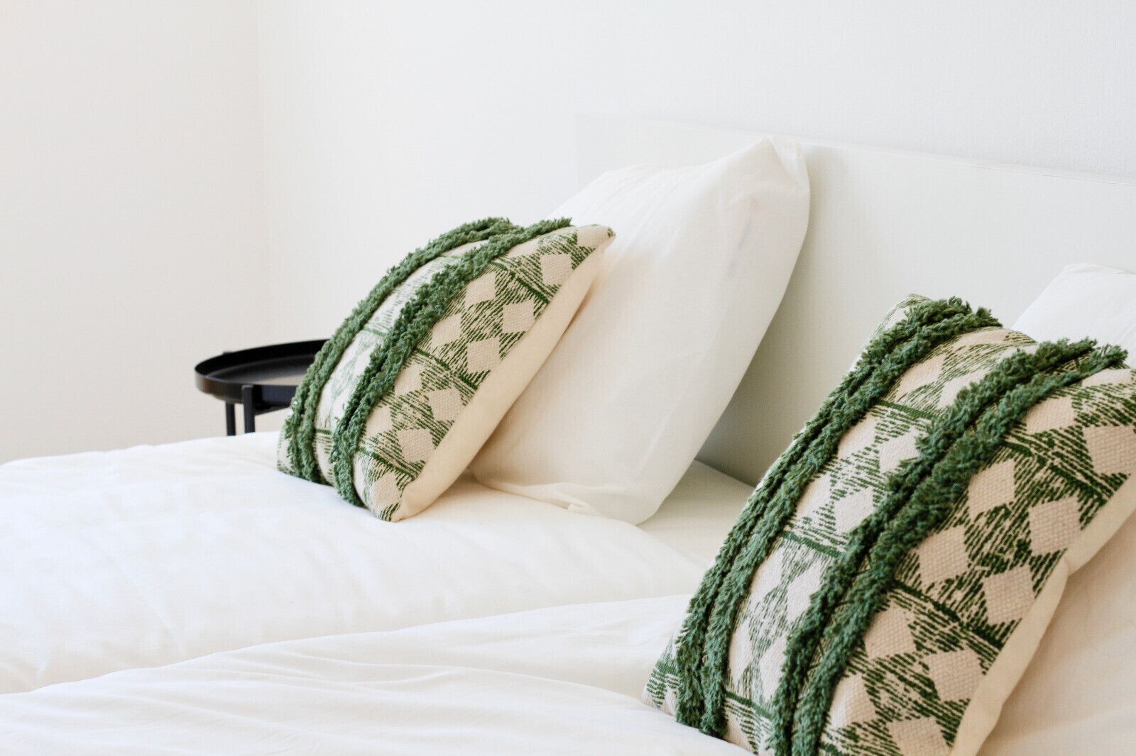 Ein Bett mit weißer Bettwäsche und zwei Kissen mit grün-beigen Mustern.