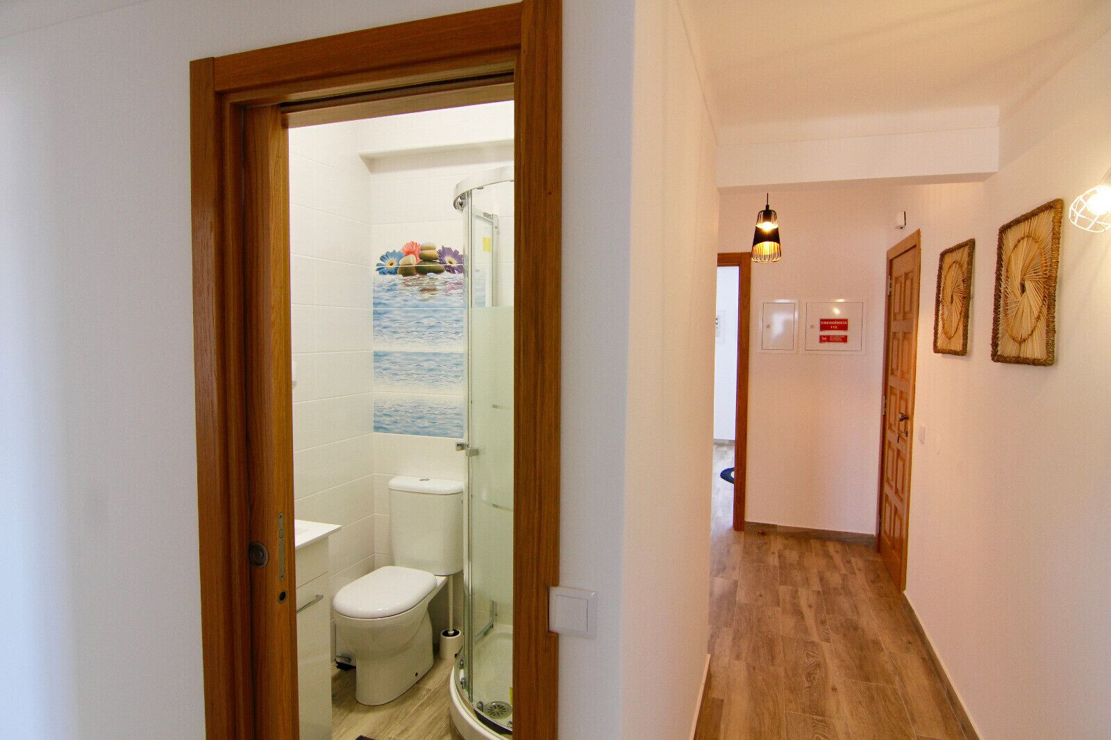 A narrow hallway leading to a bathroom with a toilet, a shower, and a glass door.