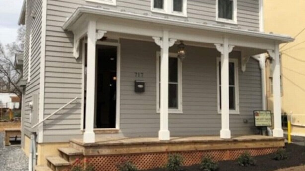A two-story house with a front porch, a mailbox, and a number plate.