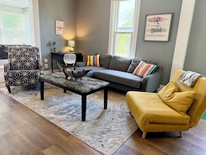 A living room with a sofa, armchair, coffee table, and decorative items. - Cozy home near DT, Premier Center: 65"TV, Foosball, Mini Golf + Fenced Yard (Sioux Falls)