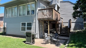 A two-story house with a covered patio area, a grill, and a small outdoor table and chairs. - Spacious 4-BR, 2.5 Bath vacation home: Foosball, 65" TV, Golf, 4 Season Room (Sioux Falls)
