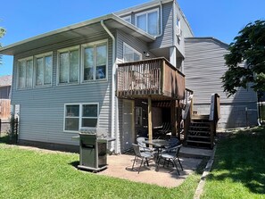 A two-story house with a covered patio area, a grill, and a small outdoor table and chairs.