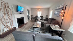 A modern living room with a fireplace, a television, and a dining area. - Spacious 4-BR, 2.5 Bath vacation home: Foosball, 65" TV, Golf, 4 Season Room (Sioux Falls)