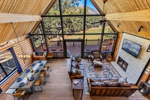 Un intérieur spacieux comprenant une longue table à manger, des sièges confortables, une cheminée et une grande fenêtre donnant sur l’extérieur.