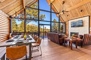 Relax in a spacious room with a high ceiling and stunning mountain views, featuring a dining area, comfortable seating, and a large framed picture.