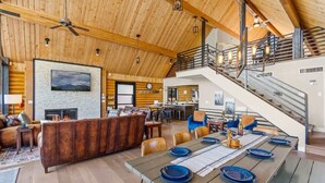 A spacious living area with a fireplace, a dining table set for four, and a staircase leading to an upper level. - Renovated | Famous Cabin | Hot Tub | AC | Mtn View (Flagstaff)