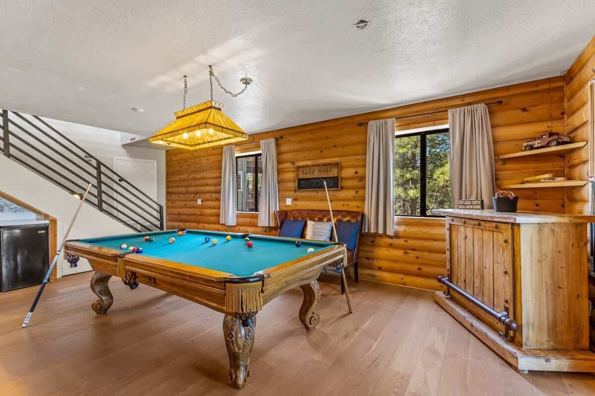 Een pooltafel in een houten chalet met een trap, een barhoek en een bord met de tekst 'let op'.