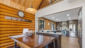 A modern kitchen with wooden walls, stainless steel appliances, and a wooden dining table with stools. - Renovated | Famous Cabin | Hot Tub | AC | Mtn View (Flagstaff)