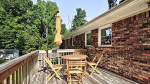 Une terrasse en bois avec une table ronde et des chaises, un mur en briques et un parasol.