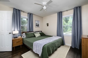 A bedroom with a bed, a nightstand, a lamp, a ceiling fan, and a window with curtains.