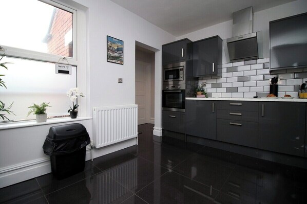 A modern kitchen with grey cabinets, a white countertop, and a black tiled floor. - Stunning sea views - Barry's Retreat by Tŷ SA (Barry)
