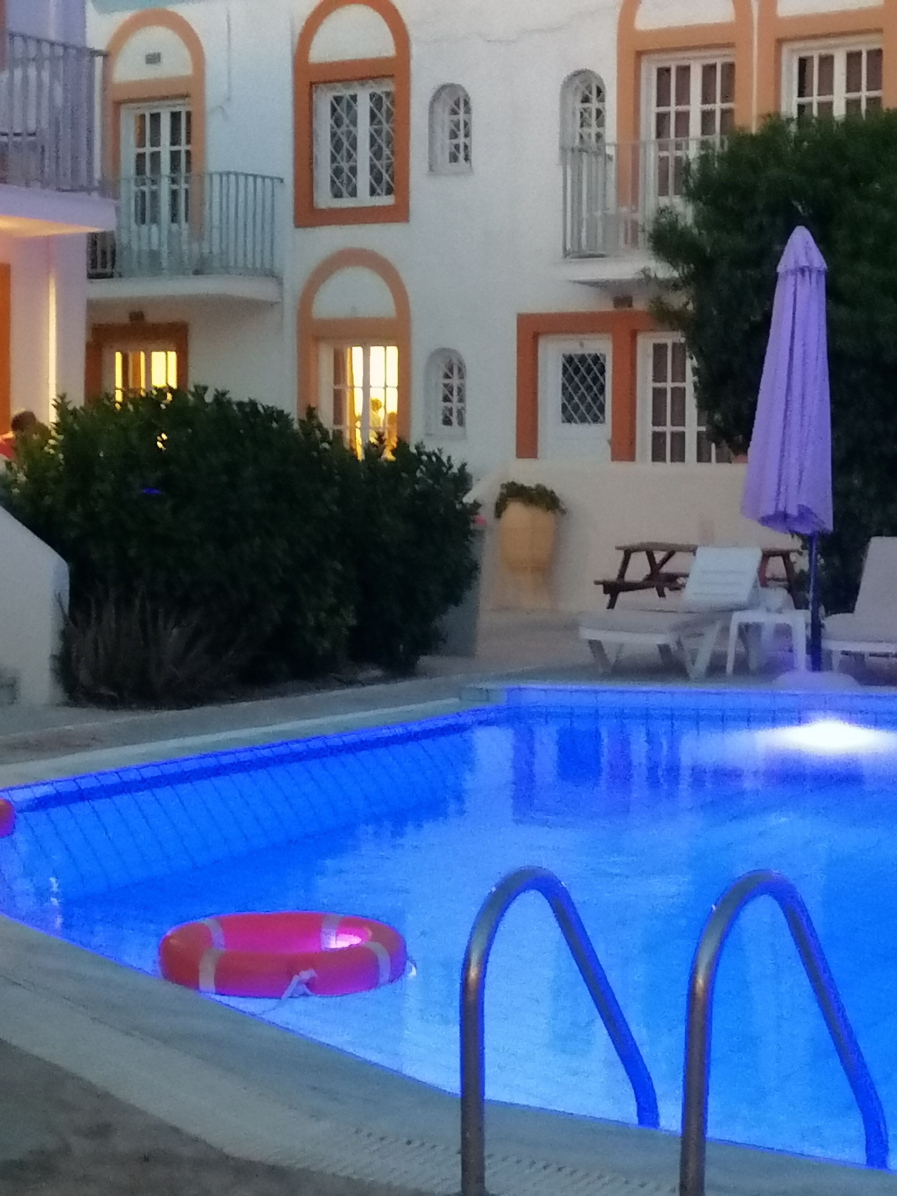 A swimming pool with a lifebuoy, a bench, and a purple umbrella.