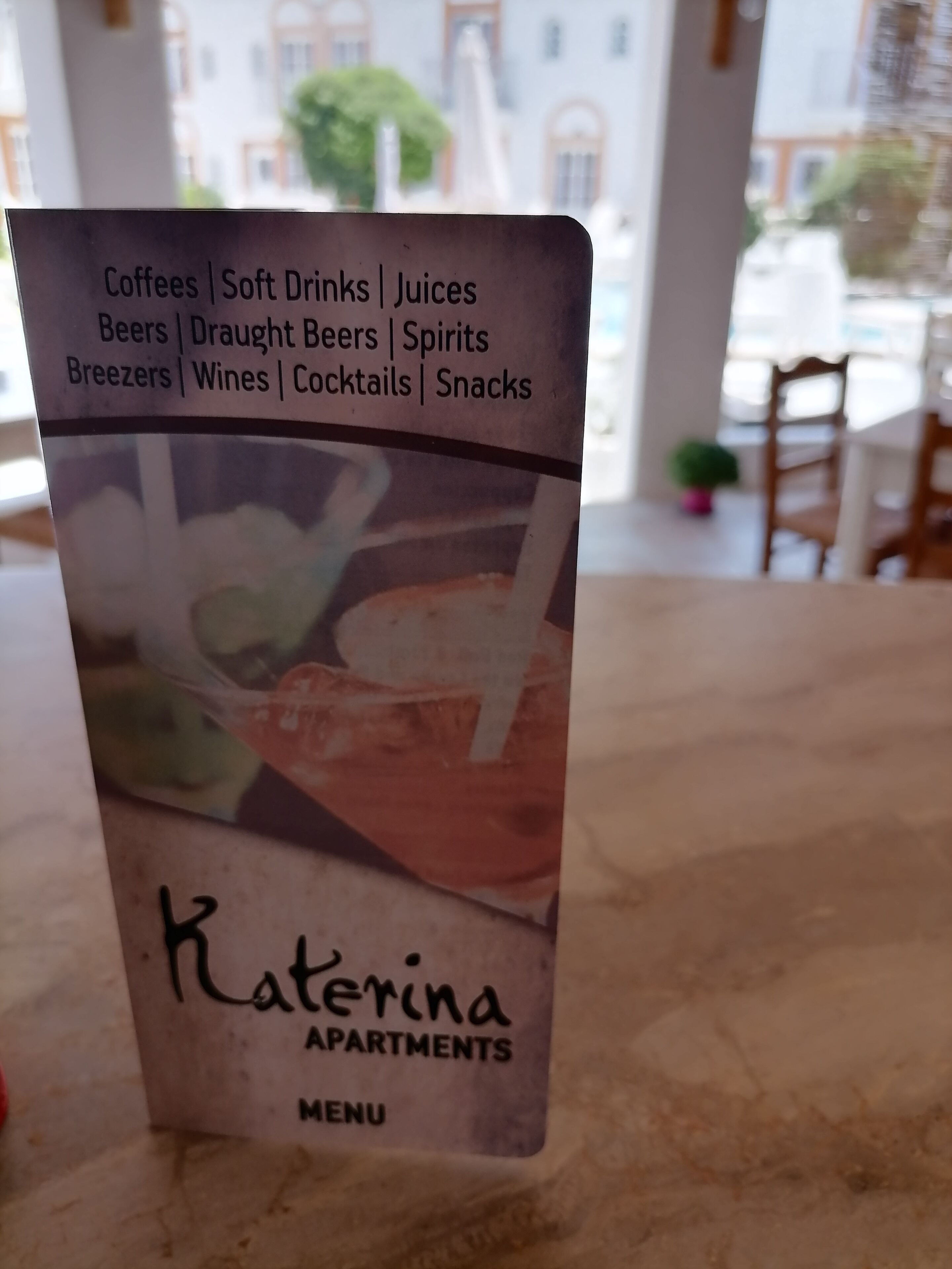 Menu fra Katerina Apartments, der viser udvalg af kaffe, sodavand, juice, øl, fadøl, spiritus, breezer, vine og snacks.