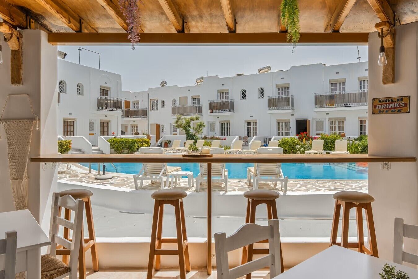 A terrace with a pool, white buildings in the background, and a sign indicating a bar area.