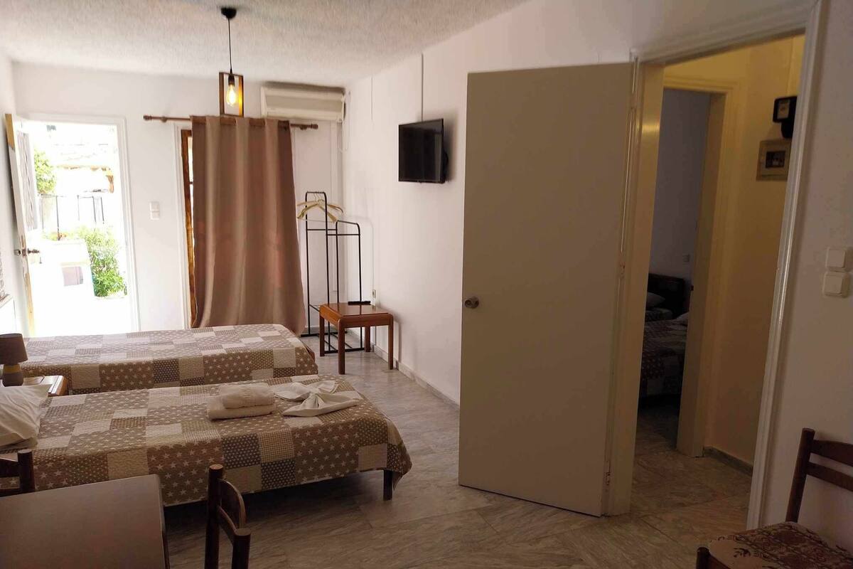 Habitación con dos camas, un televisor montado en la pared, una puerta que da a otra habitación y una mesita con una silla.