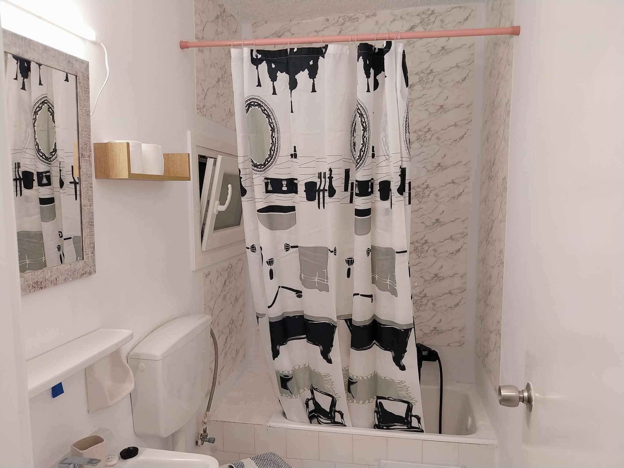 Ein Badezimmer mit Duschvorhang mit schwarz-weißen abstrakten Mustern, Toilette, Waschbecken und Spiegel.