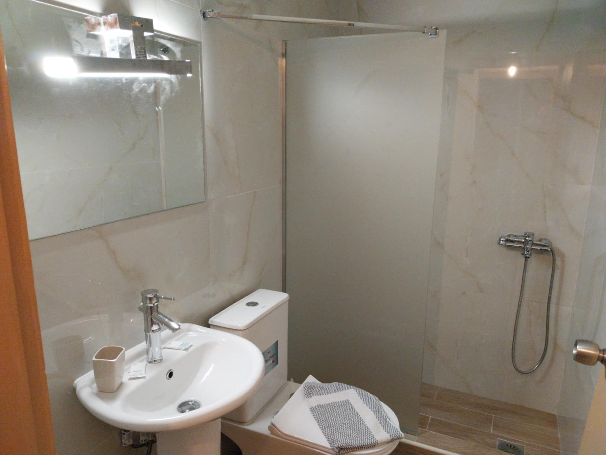 Un baño con lavamanos, espejo, inodoro y ducha.