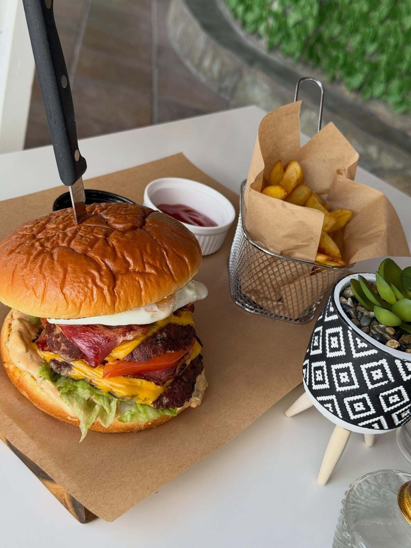 Un sándwich con un cuchillo, papas fritas, kétchup y un bol estampado sobre una mesa.