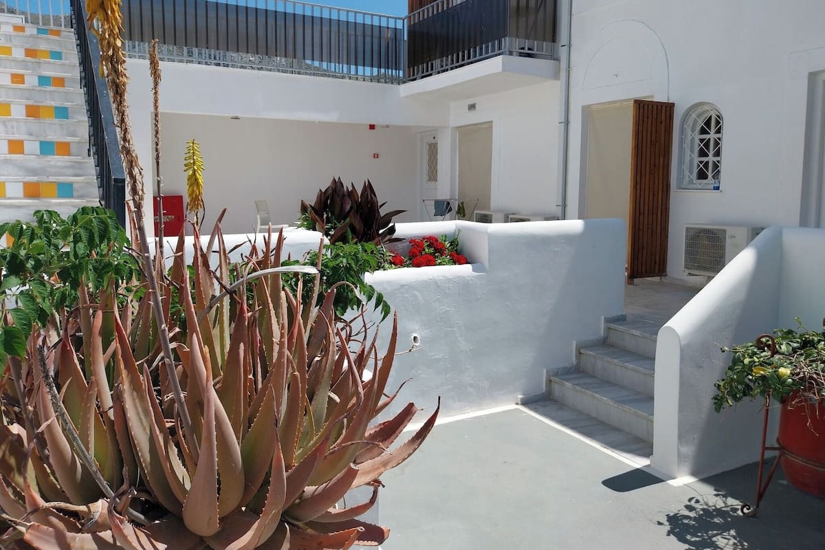 Un edificio blanco con balcón, escaleras y plantas en macetas.