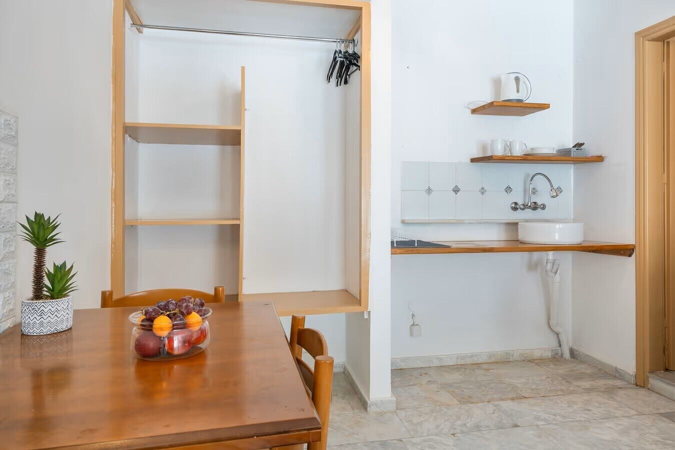 A kitchen with a wooden table, a fruit bowl, and a hanging rack.