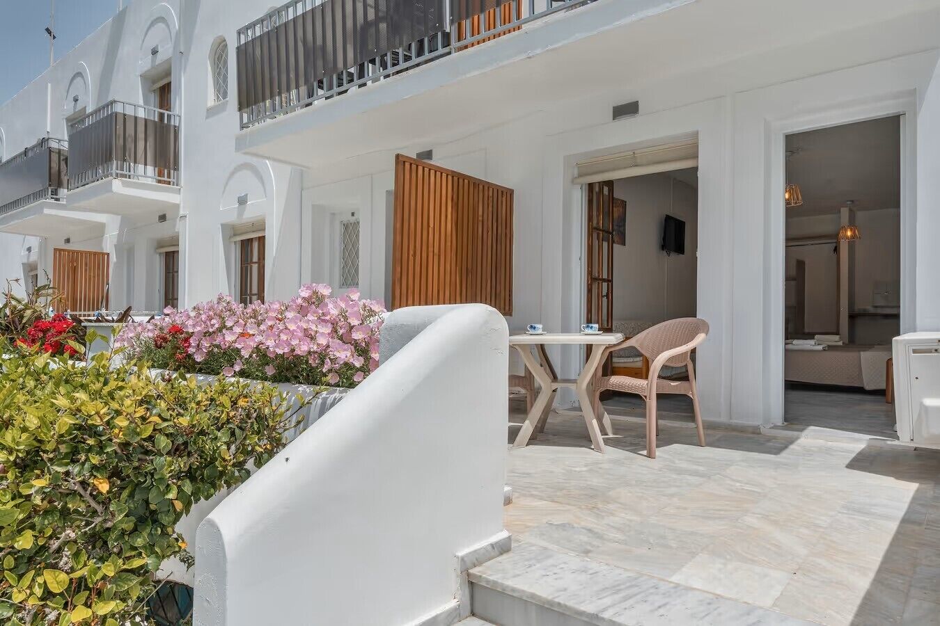 Un bâtiment blanc doté de balcons, une clôture en bois et une table avec des chaises à l’extérieur.