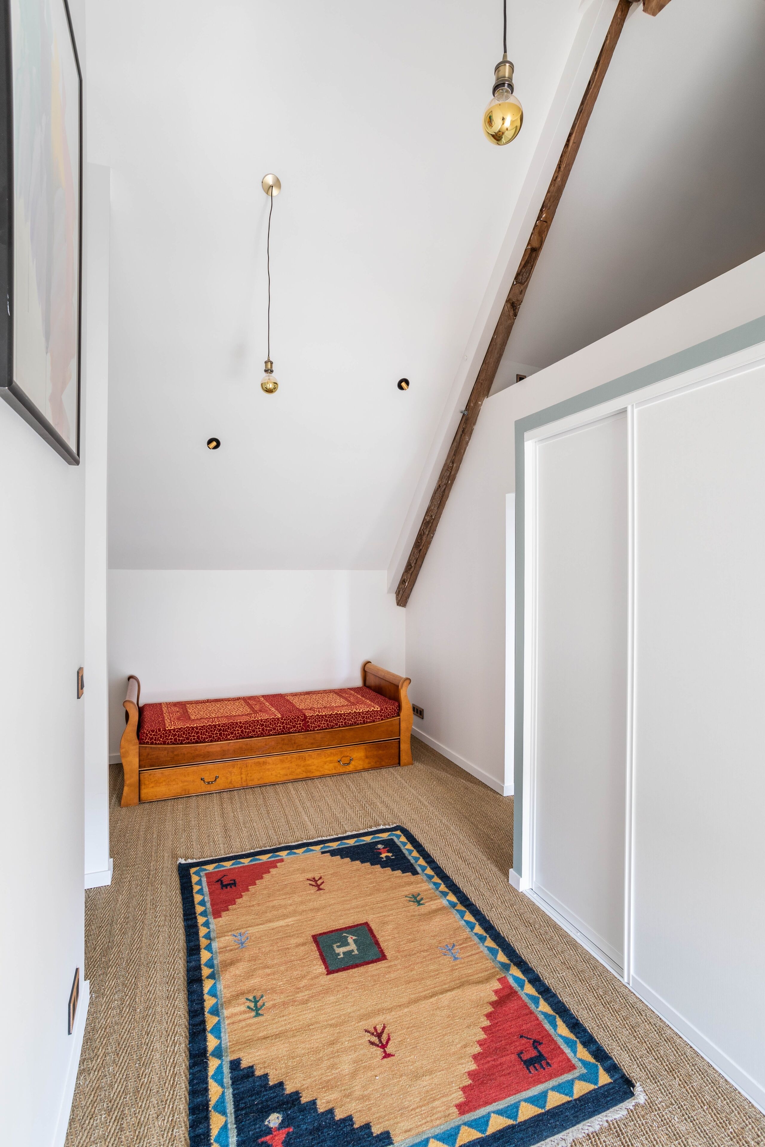 Un couloir étroit avec un banc en bois, un tapis à motifs et une porte blanche.