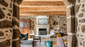 Una habitación con paredes de piedra, chimenea, vigas de madera y un rincón acogedor con sofá y sillones.