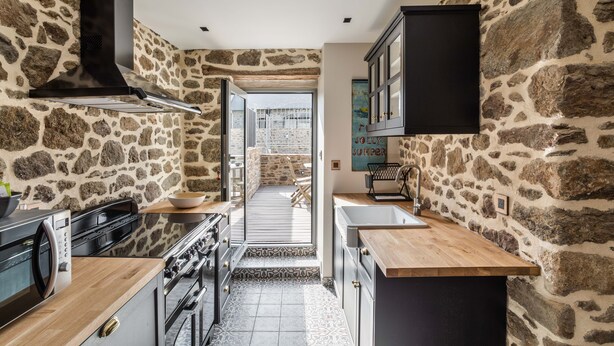 Una cocina con paredes de piedra, una campana extractora negra y vistas a un patio exterior.