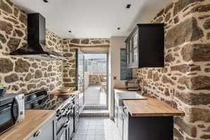 A kitchen with stone walls, a black range hood, and a view to an outdoor patio.