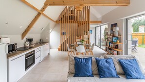 A modern kitchen with a dining area, featuring a wooden ceiling, a glass dining table, and a bookshelf with books and decorative items. - Ar Chadenn - Maison d'architecte (Saint-Cast-le-Guildo)