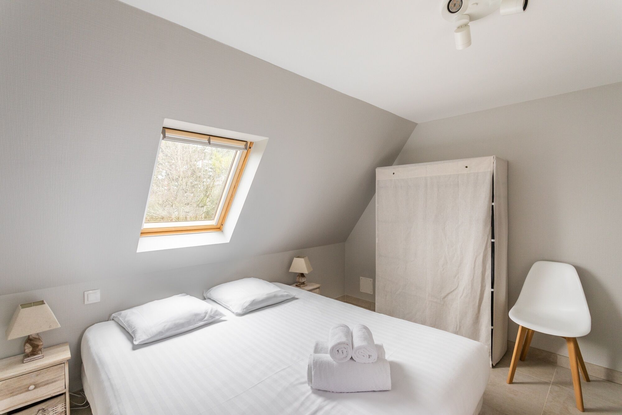Una camera da letto con un letto, un comodino, una lampada, una finestra, un armadio e una sedia.