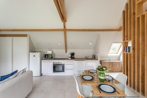A modern kitchen with white cabinets, a built-in oven, and a coffee maker. There is a dining table set with plates, glasses, and a vase with flowers. - Ar Chadenn - Maison d'architecte (Saint-Cast-le-Guildo)