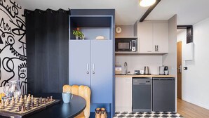 A compact living space with a dining area featuring a chessboard, a kitchen with modern appliances, and a patterned floor. - travelski home select - Résidence Yoonly & Friends - FRIENDS Studio 5 personnes (Risoul)