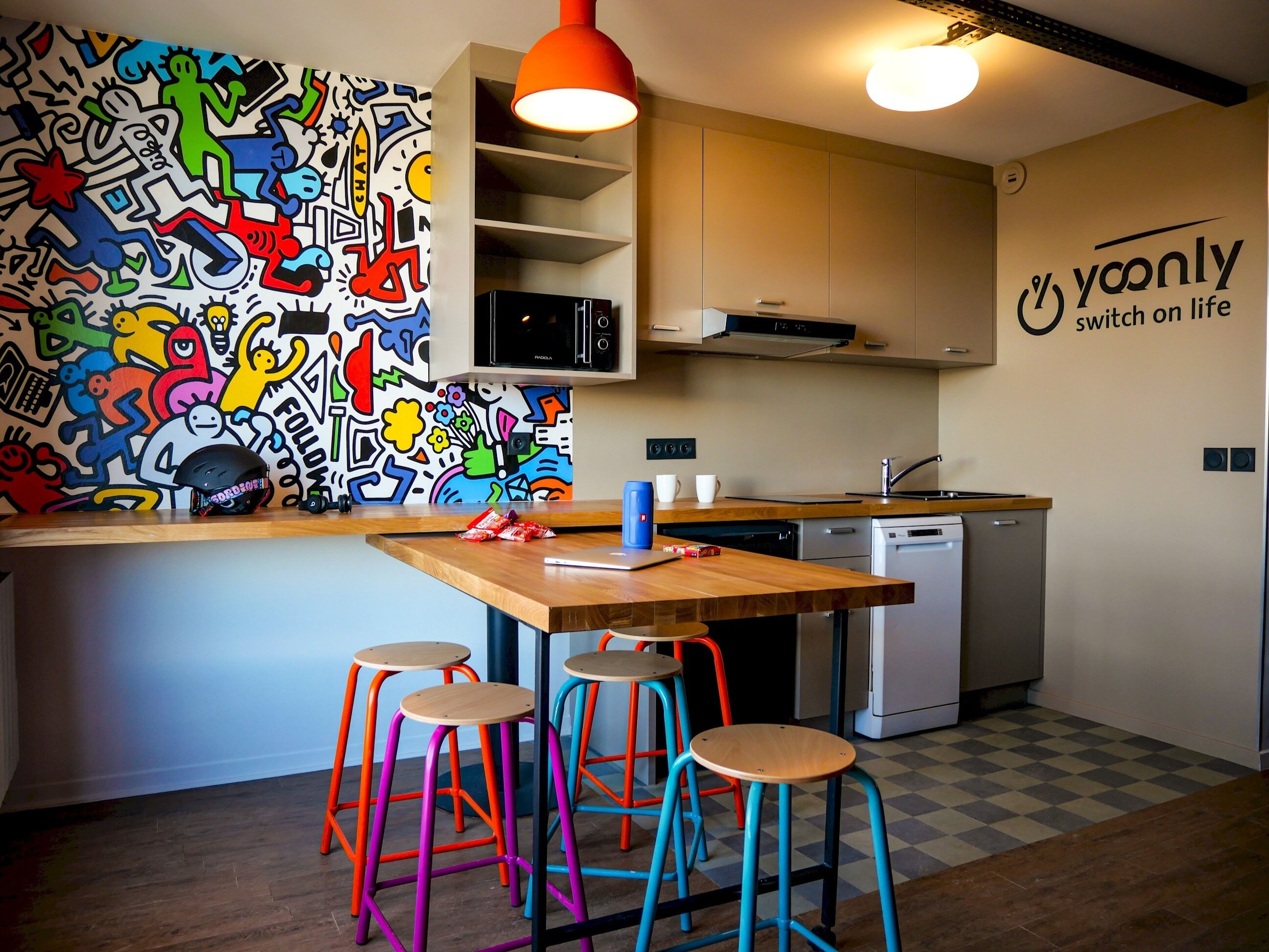 A kitchen with a colorful mural, a wooden island with stools, and a dishwasher.