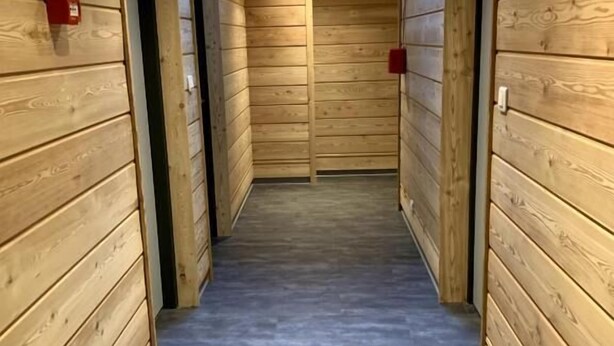A narrow hallway with wooden walls and a tiled floor, leading to a room with a skylight. - Espace Morteau (Morteau)